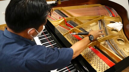 Asian man repairing the piano in a concert hall