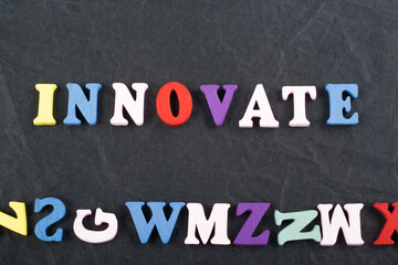 Obraz premium INNOVATEword on black board background composed from colorful abc alphabet block wooden letters, copy space for ad text. Learning english concept.