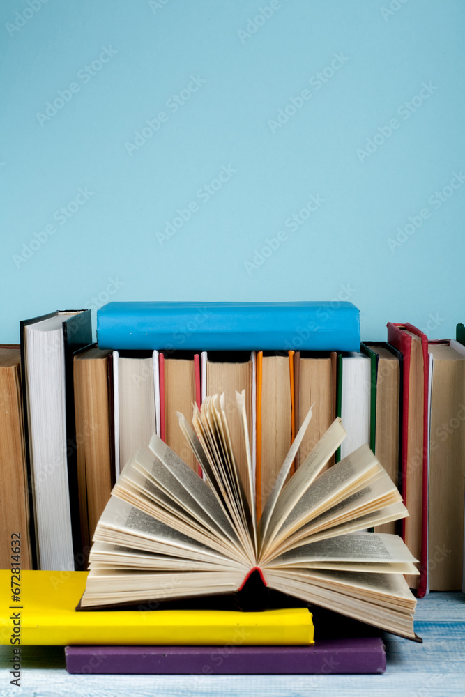 Wall mural Book stacking. Open book, hardback books on wooden table and blue background. Back to school. Copy space for text.