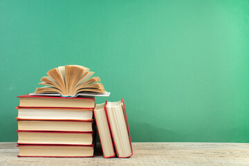 Composition with hardback books, fanned pages on wooden deck table and green background. Books stacking. Back to school. Copy Space. Education background.