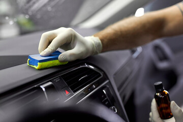 cropped male auto service worker in protective gloves, applying special polish cream on rag and polish interior of car, in renew service station shop - obrazy, fototapety, plakaty