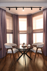 The room is cozy with curtains and a window with a table chairs and tea on the table