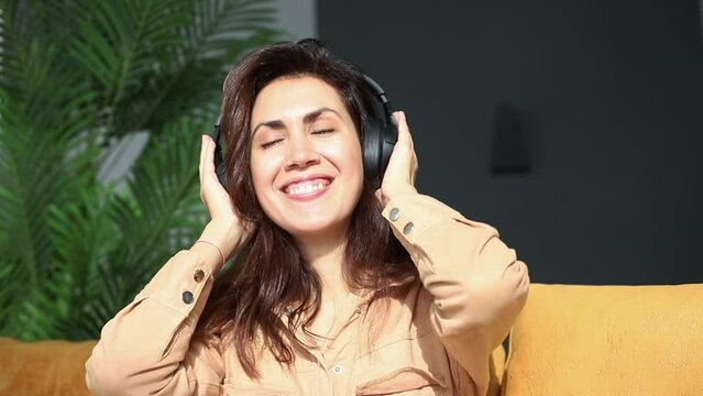 Young beautiful woman wearing headphones listening to drive music dancing sitting still on sofa in living room having fun and happy emotions