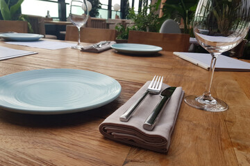 Empty flat plate, empty glass and cutlery on brown wooden table. Table setting in restaurant.