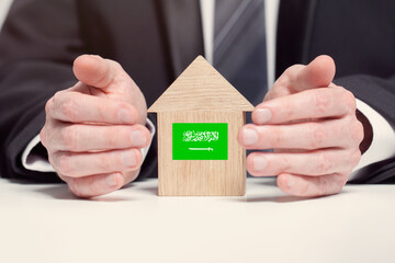 Businessman hand holding wooden home model with Saudi Arabian flag. insurance and property concepts