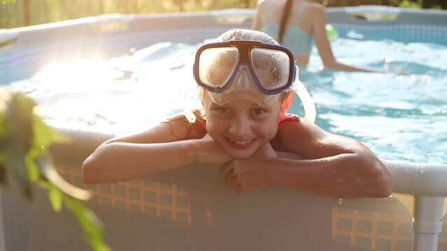 Close portrait of a young girl in a pool wearing glasses relaxing with her family in the summer at the dacha in the sunset rays. The concept of a fun summer vacation with family
