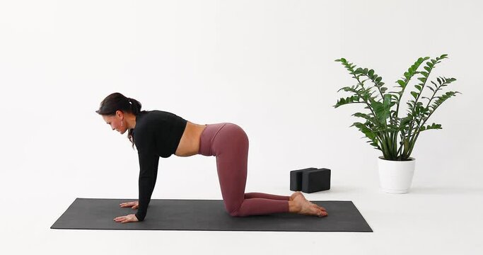 A woman leading a healthy lifestyle and practicing yoga, performs the Marjariasana exercise, cat pose with a backbend while inhaling, trains alone in sportswear in a room on a mat