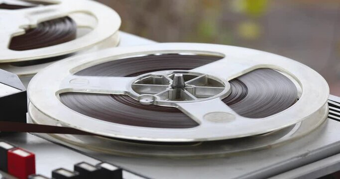 An old reel-to-reel tape recorder plays a melody, rotating reel-to-reel cassettes on a vintage music player