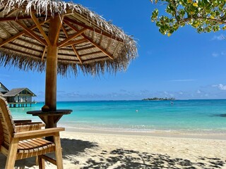 a wooden chair sits under an umbrella on a sandy beach