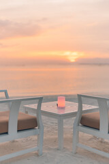 Outdoors restaurant table setting at tropical beach restaurant. Led light candles and wooden tables, chairs under beautiful sunset night sky, sea stars view. Luxury hotel or resort leisure restaurant