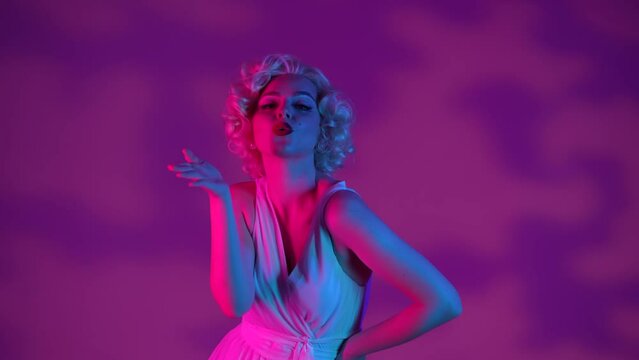Woman in look of in studio in pink and green neon light on pink background with highlights. Woman flirtatiously sends an air kiss.