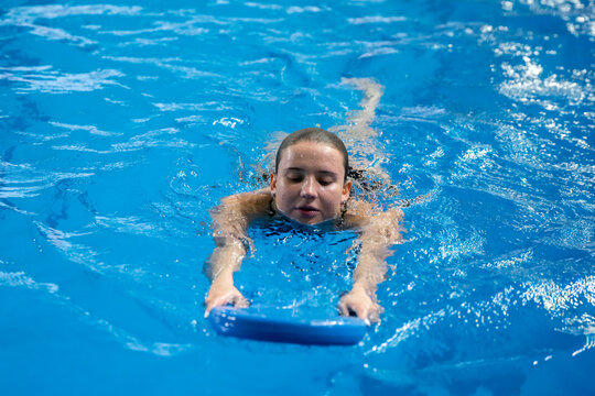 happy girl learning how to swim in the swimming pool, holding blue pool board in the water