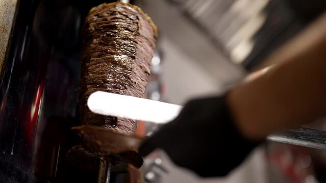 cooking national Turkish street food shawarma, cook cut meat on spit by large knife, closeup view