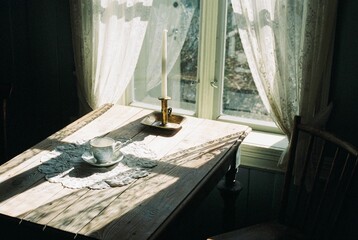 Sunlit dining table set for a meal with a vintage cup of coffee and a candle