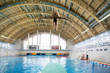 Obraz na płótnie Canvas olympic sport, sports diving in the swimming pool, female athlete doing spin in the air