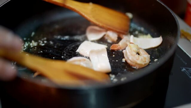 cook frying shrimps and squids with garlic on hot pan, mixing food by wooden shovels