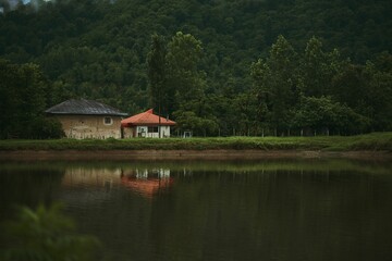 Obraz premium Scenic view of rural houses on the lakeside with lush woods in the background.