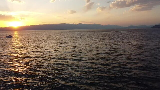 Drone footage of motorboat sailing on the sea and mountain in the background at sunset time