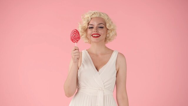 Joyful woman holding multicolored lollipop on a stick. Woman in the image of in studio on pink background. Sweet food concept.