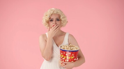 Portrait of an emotional woman crying with a big bucket of popcorn close up. Woman in the image of crying while watching a dramatic movie in studio on pink background.