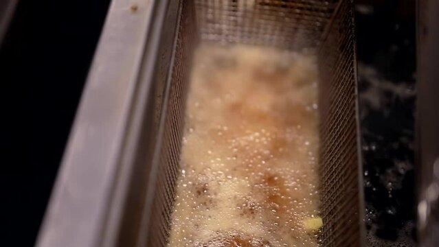 professional deep fryer in restaurant kitchen, French fries frying in boiling oil, closeup view