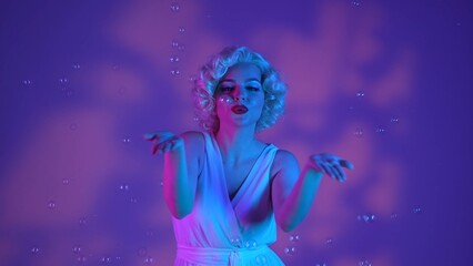 Woman dancing surrounded by soap bubbles, sending air kisses. Woman in the image of on a pink background with highlights, in a studio illuminated with pink and green neon light.