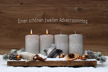 Zweiter Advent: Adventsdekoration mit zwei brennenden Kerzen vor einem braunen Holzhintergrund. Mit...