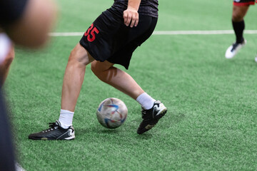 Football Futsal ball and man player legs on artificial grass field indoors.