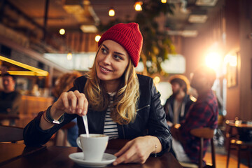 Attractive young woman stirring coffee at the cafe