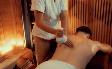 Hot herbal ball spa massage body treatment, masseur gently compresses herb bag on man body....