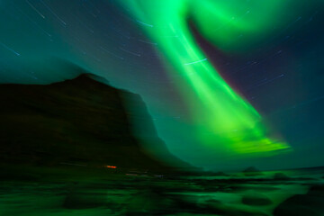 Awesome Northern lights over the beach, reflection in the silky water. Lofoten islands, Norway.