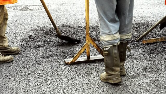 A team of workers is changing the old asphalt concrete pavement on the road. Asphalt repair in the city. A worker in special clothes and shoes performs heavy physical work. Manual labor.