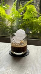 Glass of espresso on the table against green ferns