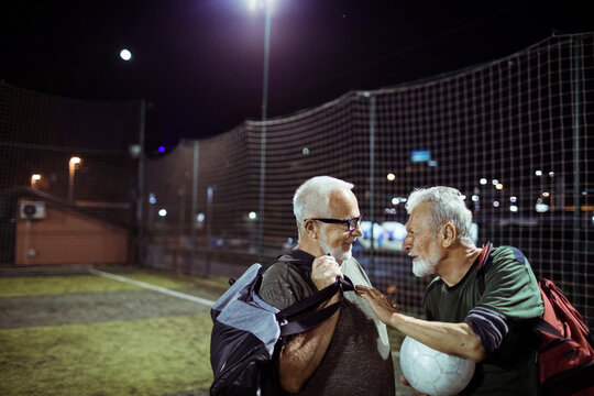Senior man holding soccer ball talking to friend