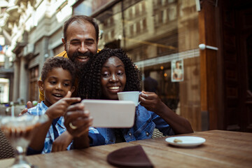 Happy multiethnic family taking selfie in outdoor cafe