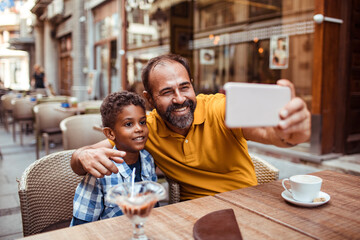 Smiling father taking selfie with son in outdoor cafe