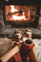Woman holding a cup of tea by the Christmas fireplace. Woman relaxes by warm fire with a cup of hot...