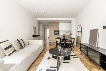 Living room of a home with an open loft-style kitchen furnished in a contemporary style with a three-seater white fabric sofa and a rug with a black marble coffee table