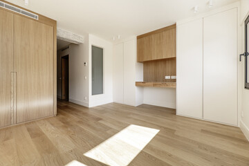 Contemporary designed bedroom with missing furniture with white wooden door and another wooden wardrobe, wall mounted desk and light wooden flooring