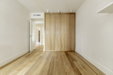 Empty bedroom with white shelves on the wall and custom-made built-in wardrobe with light oak...