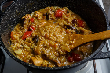 Braised eggplants with meat and rice with dogwood Israeli style in a cast-iron high frying pan with a wooden spatula.