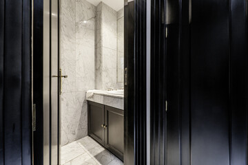 Small modern bathroom with marble tiling and countertop of the same material, black cabinet with porcelain sink and frameless mirror on the wall
