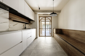 elongated kitchen with double glass and wooden doors with black lamps on the ceiling and a long bench with wooden drawers