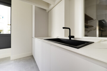 aundry room of a home with smooth white wooden furniture with a black synthetic sink with a faucet of the same color