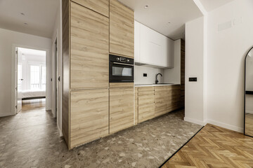 Modern open kitchen with wall covered with wooden furniture without handles, integrated black glass appliances, sink and taps of the same color and imitation marble countertop