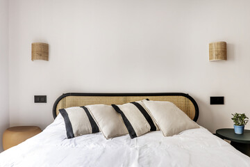 Bedroom with mesh and black wood headboard, wall lamps and disparate bedside tables
