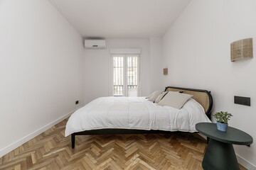 Double bedroom with large bed, matching wall lights, circular nightstand and large window with bars in the background