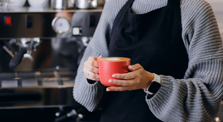 Concept production and roasting craft coffee in small workshop. Worker holds cup in front of roaster machine