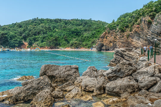 Budva, Montenegro - June 17, 2021: View from the stones to the layered rocks and Mogren beach in Budva. Delightful paradise landscape of the seashore of the Adriatic Sea in the Balkans in summer
