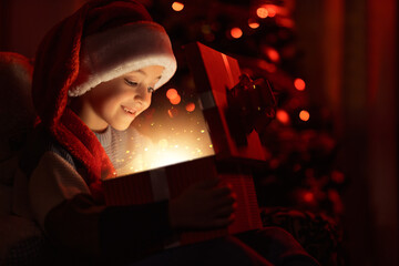 Little boy opening gifts near Christmas tree at home